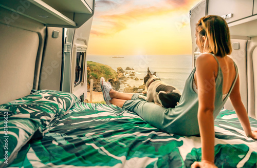 Unrecognizable young woman with her boston terrier dog watching the sunset sitting on the bed of her camper van