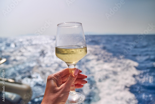 hand with glass of white wine with sea or ocean on background photo