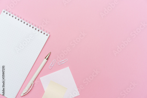 Workspace concept for school or office. Flat lay with an open notebook on a spring, a white color pencil, a plastic clip on paper background colors pink with copy space.