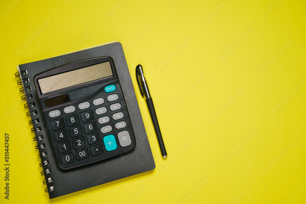 Notepad on spring black calculator and ballpoint pen on yellow background, business and accounting concept Notepad on spring black calculator and ballpoint pen on yellow background, business and accounting concept