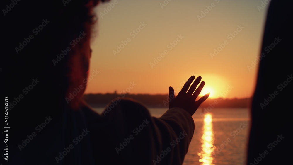 Girl stretching hand silhouette in golden sunlight posing rear view close up.