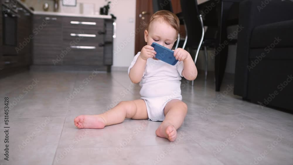 Cute baby holds phone in hands. The child plays with cell phone, examines it, tugs in his hands and tries to eat smartphone putting it in his mouth. Cute baby holds phone in hands. The child plays with cell phone, examines it, tugs in his hands and tries to eat smartphone putting it in his mouth.
