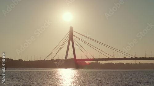 River bridge silhouette at clear sky summer day. Water reflect golden sunlight 