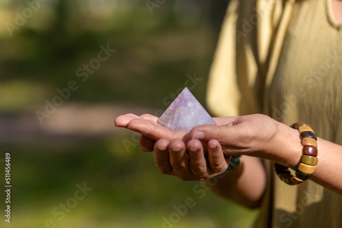 occult science and supernatural concept - close up of woman or witch with semiprecious crystal or gemstone pyramid performing magic ritual in forest