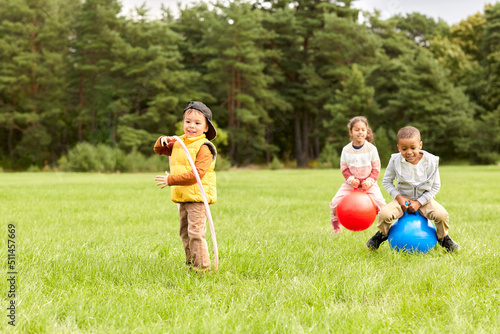 childhood, leisure and people concept - group of happy children playing with hopper balls and hula hoop at park photo