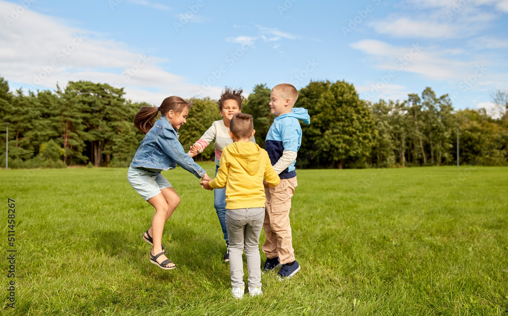 childhood, leisure and people concept - group of happy kids playing round dance at park childhood, leisure and people concept - group of happy kids playing round dance at park