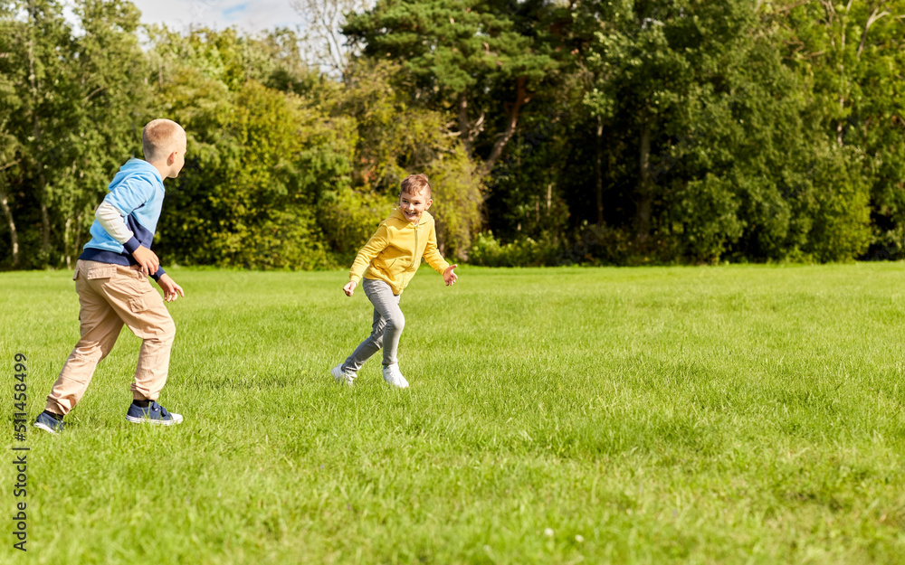 childhood, leisure and people concept - two happy boys playing tag game and running on lawn at park