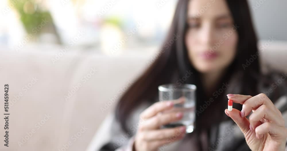 Woman on the couch, holding a capsule and a glass of water Woman on the couch, holding a capsule and a glass of water