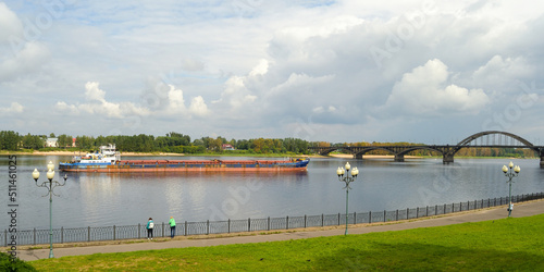 Tourists on the embankment look at a ship and a cargo barge on the Volga river in the city of Rybinsk, Russia.