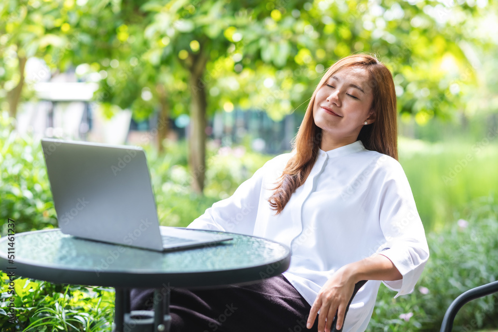 Portrait image of a woman with closed eyes, sitting and relaxing while working on laptop computer in the park Portrait image of a woman with closed eyes, sitting and relaxing while working on laptop computer in the park
