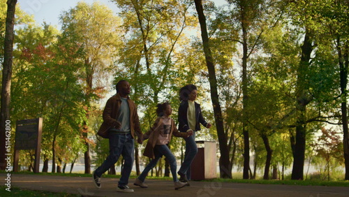 African american family walk autumn park together. Happy kid hold parents hands.