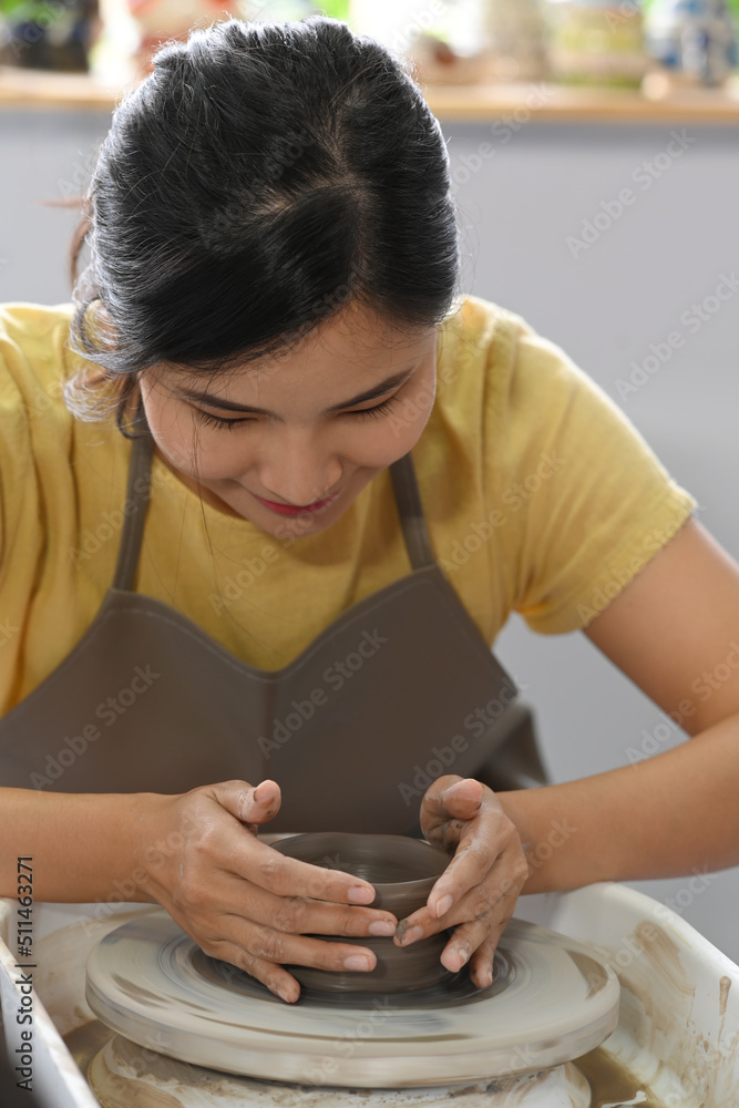 Concentrated young woman is creating handicraft crockery on the pottery wheel in art workshop. Pottery working, handmade clay products Concentrated young woman is creating handicraft crockery on the pottery wheel in art workshop. Pottery working, handmade clay products