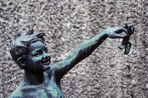 La statua di bronzo ossidato di un bambino sorridente che tiene in mano un granchio sopra una tomba del cimitero monumentale di Milano photo