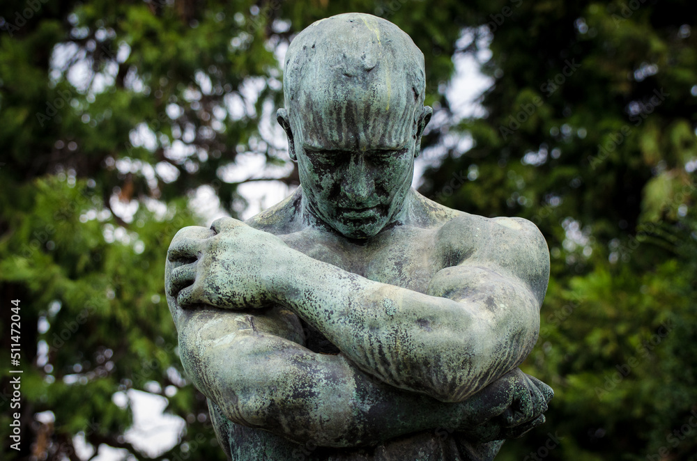 La statua di bronzo ossidato di un uomo sofferente sopra una tomba del cimitero monumentale di Milano