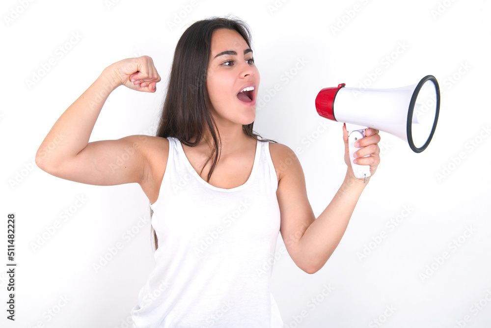 Young beautiful brunette woman wearing white top over white wall communicates shouting loud holding a megaphone, expressing success and positive concept, idea for marketing or sales. Young beautiful brunette woman wearing white top over white wall communicates shouting loud holding a megaphone, expressing success and positive concept, idea for marketing or sales.