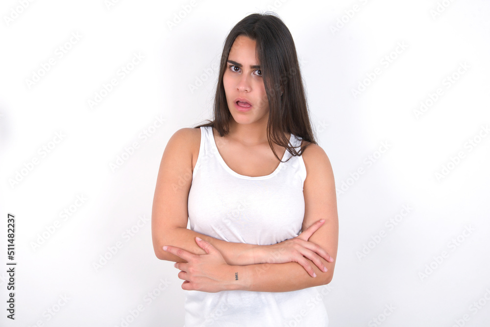 Shocked embarrassed young beautiful brunette woman wearing white top over white wall keeps mouth widely opened. Hears unbelievable novelty stares in stupor Shocked embarrassed young beautiful brunette woman wearing white top over white wall keeps mouth widely opened. Hears unbelievable novelty stares in stupor