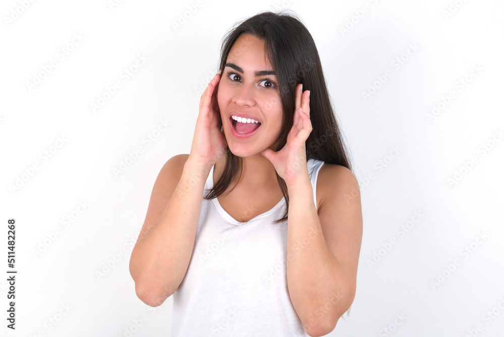 young beautiful brunette woman wearing white top over white wall Pleasant looking cheerful, Happy reaction young beautiful brunette woman wearing white top over white wall Pleasant looking cheerful, Happy reaction