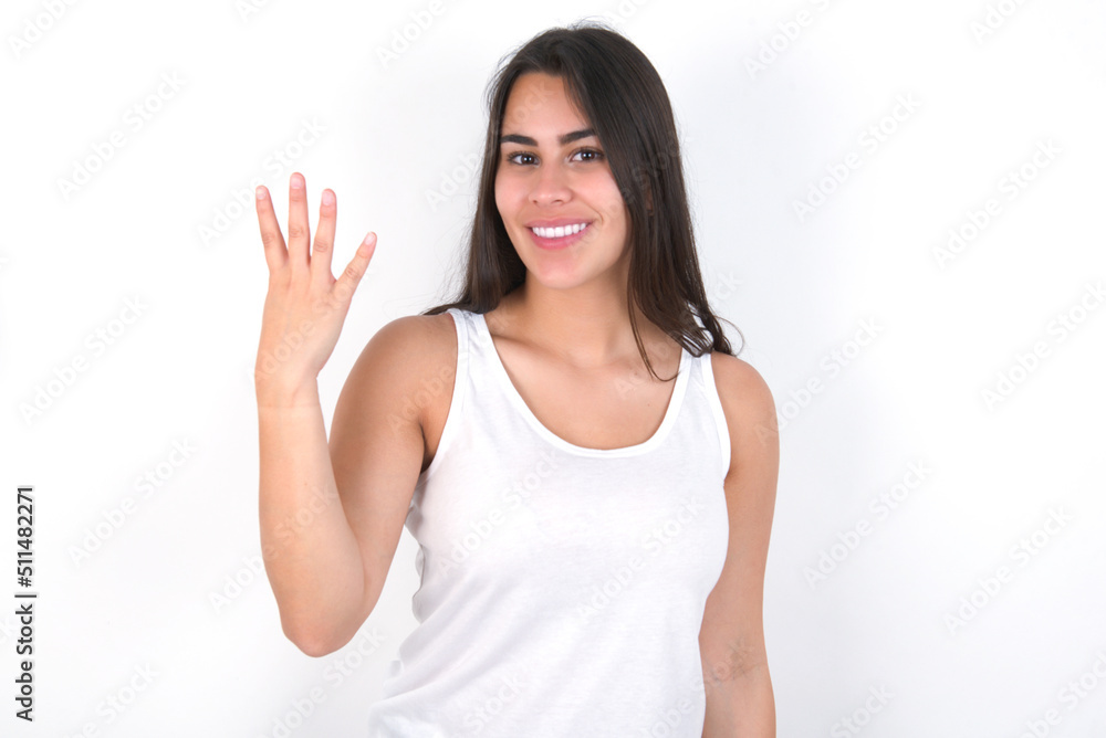 young beautiful brunette woman wearing white top over white wall smiling and looking friendly, showing number four or fourth with hand forward, counting down young beautiful brunette woman wearing white top over white wall smiling and looking friendly, showing number four or fourth with hand forward, counting down