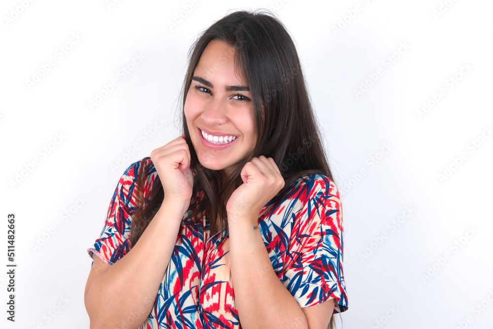 young beautiful brunette woman wearing colourful dress over white wall grins joyfully, imagines something pleasant, copy space. Pleasant emotions concept. young beautiful brunette woman wearing colourful dress over white wall grins joyfully, imagines something pleasant, copy space. Pleasant emotions concept.