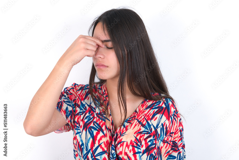 Sad young beautiful brunette woman wearing colourful dress over white wall suffering from headache holding hand on her face Sad young beautiful brunette woman wearing colourful dress over white wall suffering from headache holding hand on her face