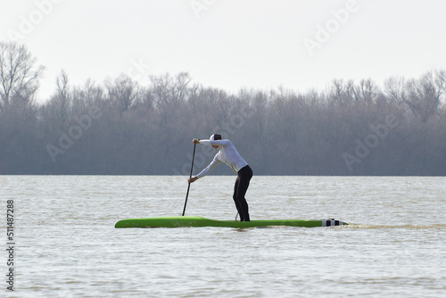 Athletic man paddleboarding on stand up paddle board on the winter river