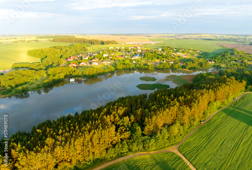 River near village  aerial view. Green fields and forest in rural. Country houses at river in countryside  drone view. Village with wooden house. Suburban house in rural on sunrise.