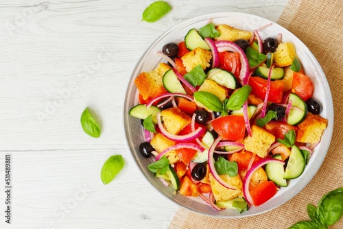 Italian Traditional Dish"Panzanella",mixed salad with tomatoes,breads,cucumbers,red onions,olives,basil,olive oil,salt and peppers on plate with wooden background.Fresh and healthy vegetarian salad