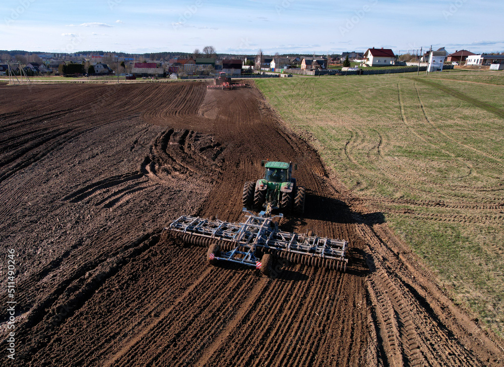 Obraz premium Tractor with cultivator plowing field. Tractor disk harrow on ploughing a soil. Planting in farmland. Sowing seed on plowed field. Seeding in agriculture. Farm Machinery for cultivating. Tractor plow.