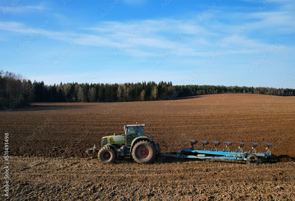 Obraz premium Tractor plow soil cultivating. Green Tractor plowing field. Cultivated land and soil tillage. Agricultural tractor on farm field cultivation. Tractor disk harrow plowing farm field. .