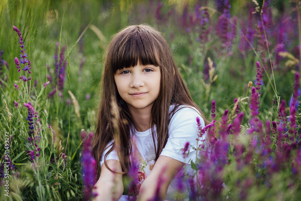 Pretty girl 7-8 years old, sitting in the lavender field, looking at the camera Pretty girl 7-8 years old, sitting in the lavender field, looking at the camera