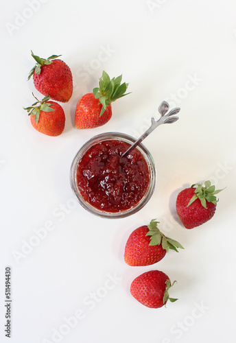 Homemade strawberry preserves or jam in a mason jar surrounded by fresh organic strawberries. Selective focus with white background.