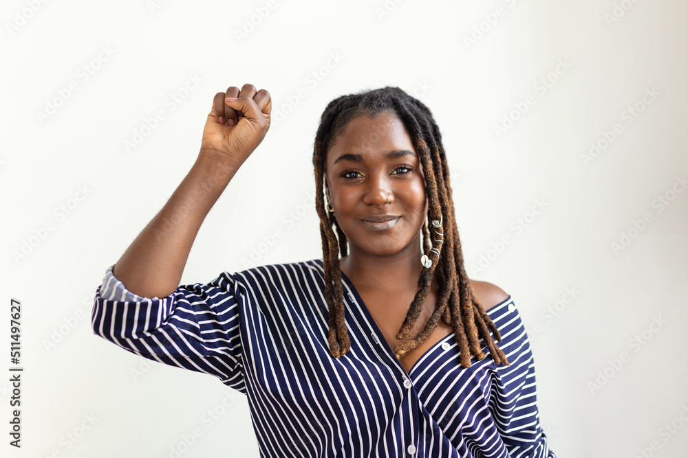 Raised hand of young African woman clenched into fists on light background. Stop racism concept Raised hand of young African woman clenched into fists on light background. Stop racism concept