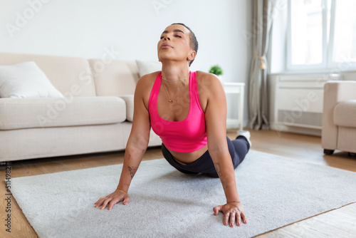 Relief Lower Back Pain. Smiling Black Woman Doing Sphinx Cobra Pose Or Upward-Facing Dog Asana Stretching Back Muscles Practicing Pilates, Excercising At Fitness Studio Or In Living Room On Yoga Mat