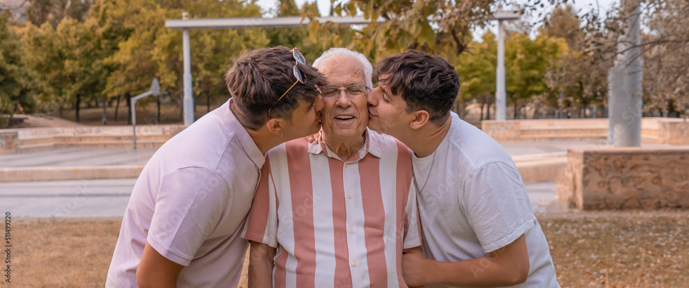 Dos nietos besando a su abuelo en el parque, con expresión cariñosa y felices. Fotografía en horizontal. Dos nietos besando a su abuelo en el parque, con expresión cariñosa y felices. Fotografía en horizontal.