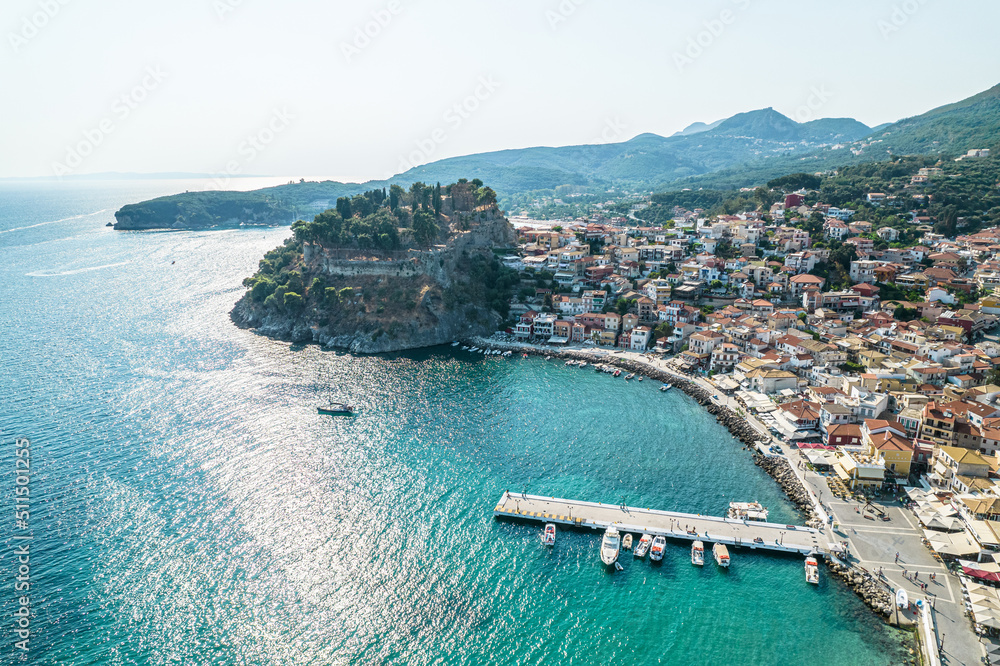 Beautiful colorful houses of seaside town, port of Parga with boats, cruise ship. Sand beach with umbrellas, tourist people, blue, turquoise sea water. Summer vacations and travel concept. Greece