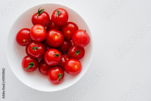 Top view of fresh cherry tomatoes in bowl on white background. © LIGHTFIELD STUDIOS