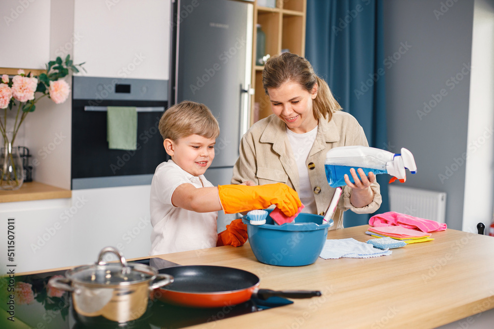 Little boy and his mother doing cleaning in a kitchen using a detergents Little boy and his mother doing cleaning in a kitchen using a detergents