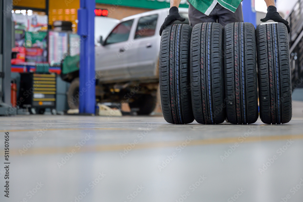 Fototapeta premium male tire changer In the process of bringing 4 new tires that are in stock in order to change the wheels of the car at a service center or an auto repair shop for the automobile industry