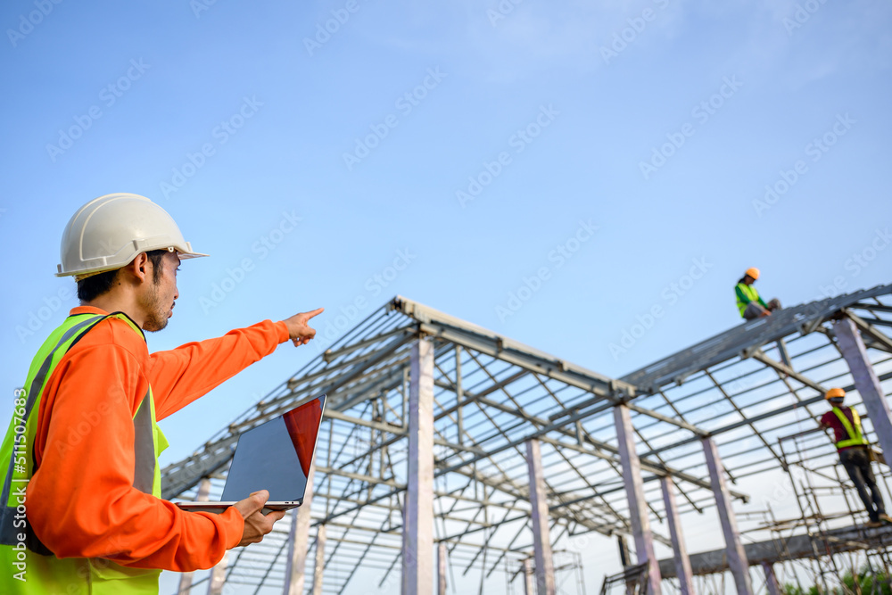 male construction engineer holding laptop standing at a house construction site Controlling and ordering Construction workers for quality inspection and steel roof truss design plans male construction engineer holding laptop standing at a house construction site Controlling and ordering Construction workers for quality inspection and steel roof truss design plans