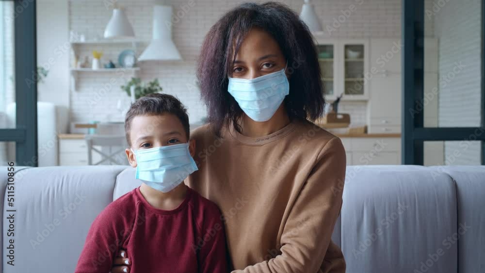 Close-up. Single mother sitting next to her son, hugging him tenderly, wearing protective medical surgical mask. Self-isolation concept, prevention of seasonal infectious viral and bacterial diseases.