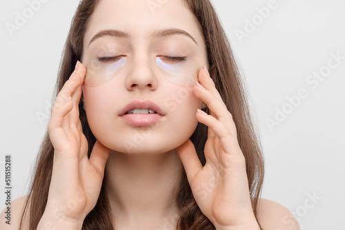 Close up shot of a young woman applying eye pads. Eyes closed, gently touches her face.