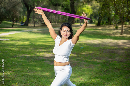Beautiful Indian young woman doing workout with hula hoop in the park outdoor, Happy asian female do acrobat, sports and Fitness concept.