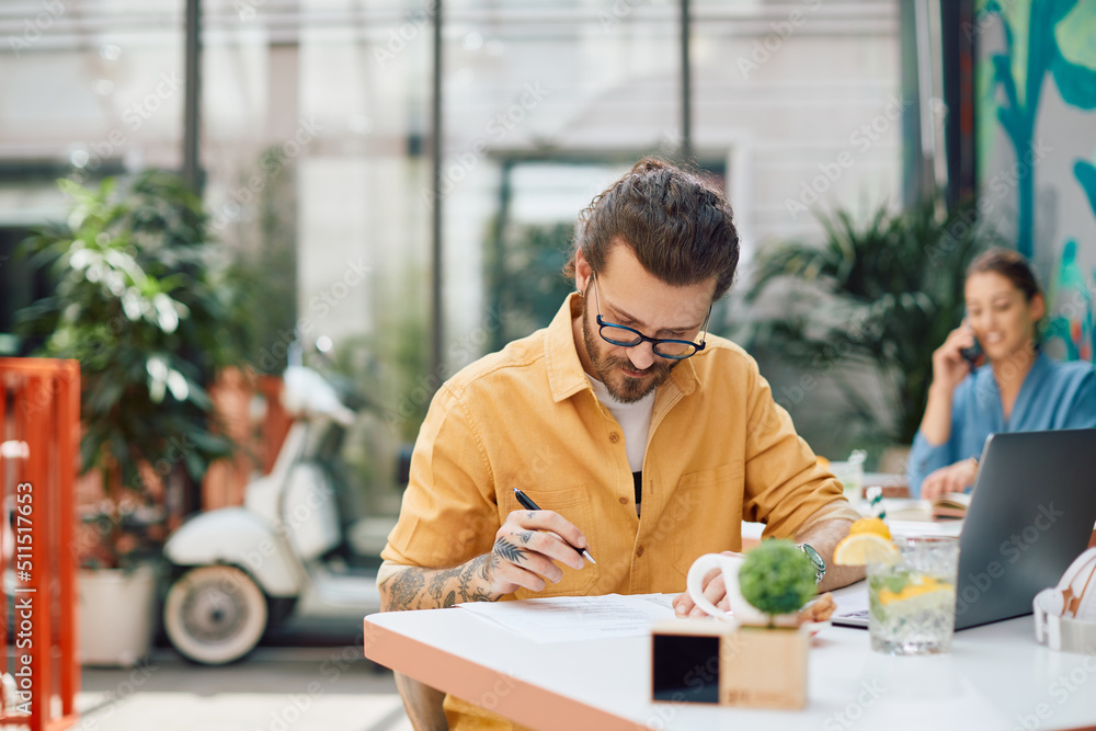 Fototapeta premium Young businessman going through paperwork while working in cafe,