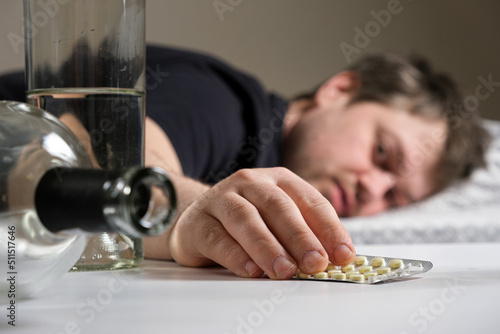 A man lies on a bed after an alcohol party, holding hangover pills in his hand