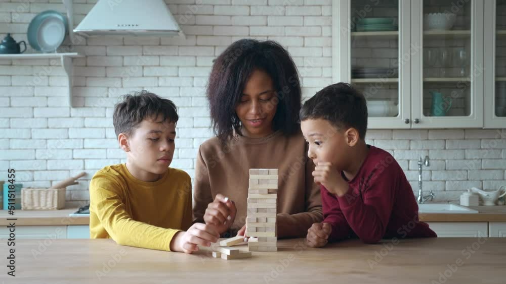 African American ethnicity mom and children playing the falling tower, sitting at the table in the kitchen. Family of a single mother and two adorable boys sons, enjoying educational games at home African American ethnicity mom and children playing the falling tower, sitting at the table in the kitchen. Family of a single mother and two adorable boys sons, enjoying educational games at home