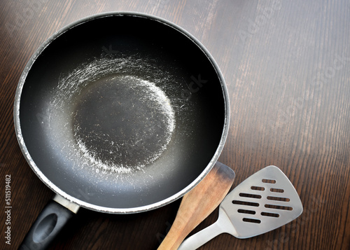 Old scratched non-stick pan on wood table. Teflon pan peeling off. Copy space is on the right side. 
