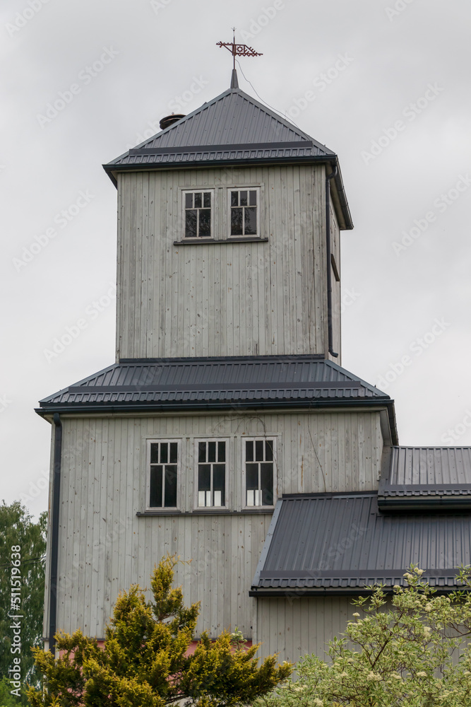 Durbe city firefighter building, tower. wooden building, metal roof, wind indicator. green trees, cloudy sky