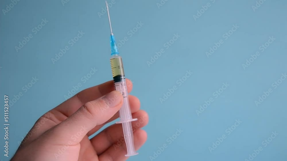 Doctor's hand holds a syringe with vaccine or antibiotic on blue background. Health and medical concepts Doctor's hand holds a syringe with vaccine or antibiotic on blue background. Health and medical concepts