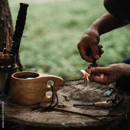Fotografiet Man´s hand sparkling a ferro rod with a wooden cup with coffee