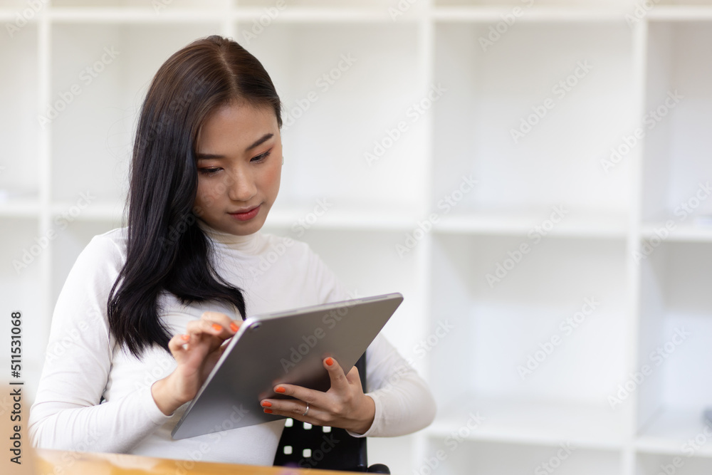 Attractive young Asian business woman wearing casual clothes is working on a tablet in the home office. Attractive young Asian business woman wearing casual clothes is working on a tablet in the home office.